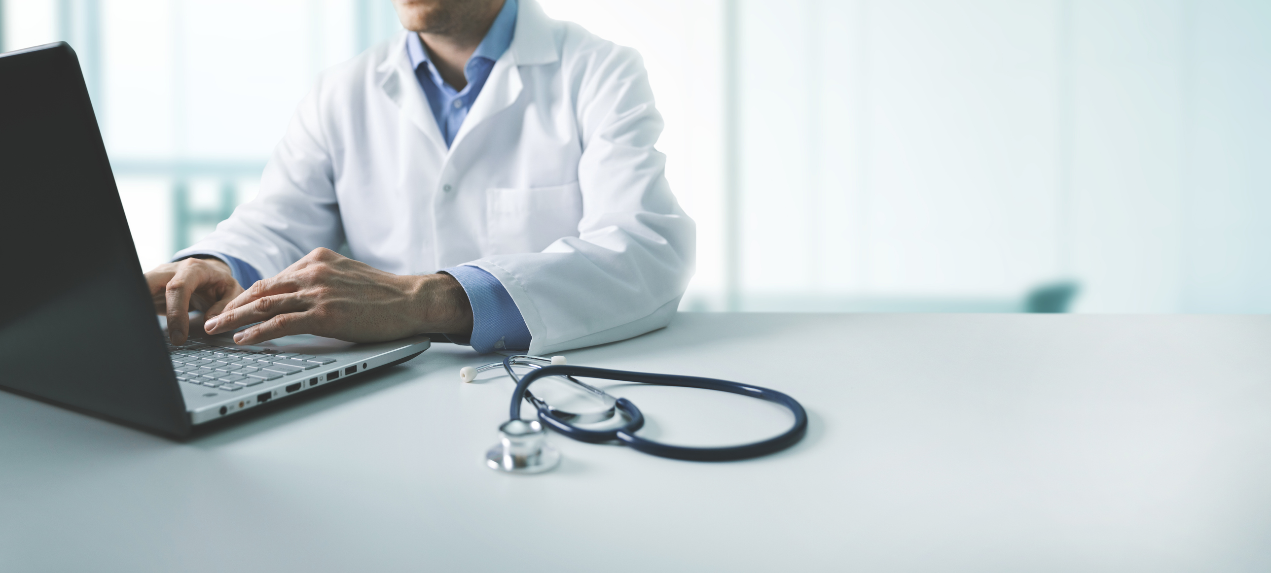 Doctor in white coat typing on laptop